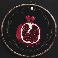 an embroidered pomegranate is displayed on a black surface with red beads around it