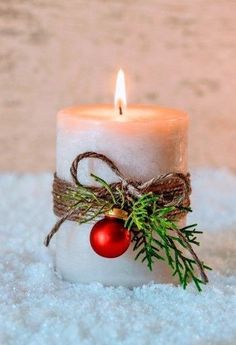 a white candle with a red ornament sitting on top of it in the snow