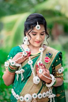 a woman in green and gold sari with beads around her neck, holding something