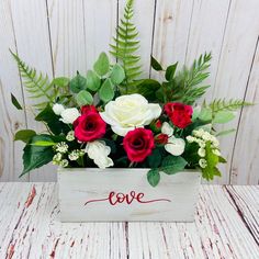 a bouquet of roses in a wooden box with the word love written on it and greenery