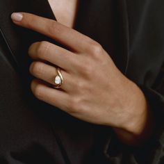 a woman's hand wearing a gold ring with a white diamond in the middle