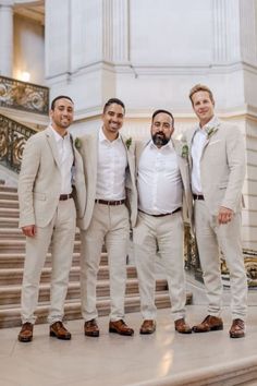 three men standing next to each other in front of some stairs with one man wearing a white shirt and tan suit