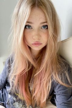 a woman with long blonde hair and blue eyes is sitting on a couch looking at the camera