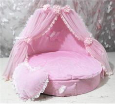 a pink bed that is on top of a white table and has a heart shaped pillow next to it