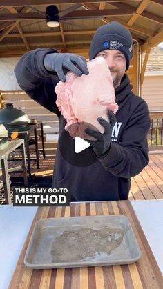 a man holding up a piece of meat on top of a wooden table next to a pan