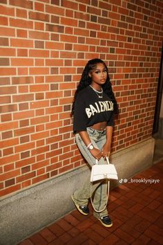 a woman standing in front of a brick wall holding a white purse and looking at the camera