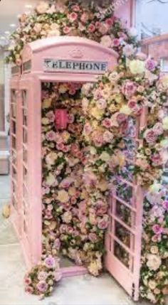 a pink phone booth covered with flowers and greenery in a mall or shopping center