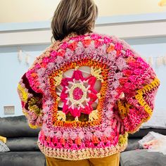 a child wearing a crocheted jacket with flowers on it's back and shoulders