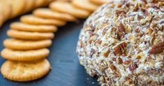 a cheese ball covered in nuts next to crackers on a black surface with other snacks