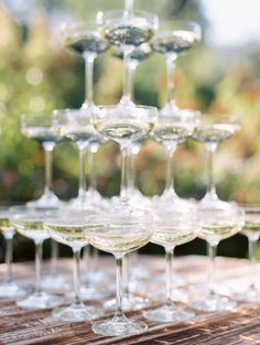 several wine glasses are lined up on a wooden table outside with trees in the background