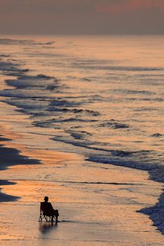 a person sitting in a chair on the beach watching the sun rise over the ocean