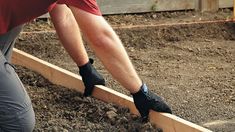 a man in red shirt and black pants working on a garden bed with wooden boards