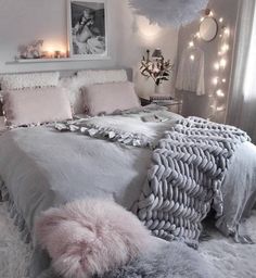 a white bedroom with fluffy pillows and blankets on the bed, lights in the background