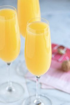 two glasses filled with orange juice on top of a white tablecloth next to a spoon