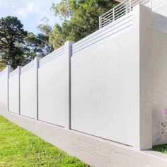 a white fence in front of a house with pink flowers growing on the grass next to it