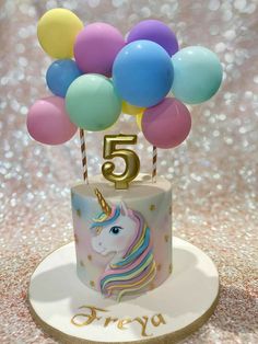 a unicorn birthday cake with balloons and the number five