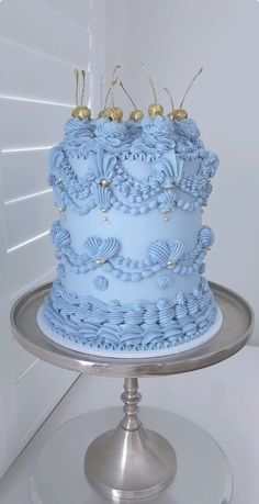 a blue cake sitting on top of a silver plate covered in frosting and gold decorations