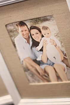 a couple holding a baby and posing for a picture in front of a white frame