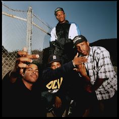 four young men posing for a photo in front of a chain link fence with one pointing at the camera