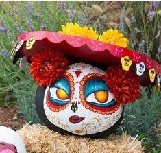 a decorated rock with flowers on it sitting next to a ball in the grass and some plants