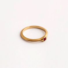 Our round ruby engagement gold ring is a dainty ring with a small ruby set within it. The ring is part of the 'Strings' ring family, a series of rings with a triangular profile and a small stone set in a variety of ways. They stack together gently, with small airy spaces between them, and can be suitable as engagement rings. The ring is made using traditional jewelry techniques to create a piece of jewelry that is classic and unique. It is elegant and comfortable to wear and will live with you h Gold Stackable Rings With Ruby Bezel Setting, Gold Stackable Ruby Ring, Gold Stackable Ruby Birthstone Ring, Ruby Stackable Round Band Promise Rings, Ruby Ring With Round Band For Promise, Gold Ruby Rings With Round Band, Yellow Gold Ruby Promise Ring With Birthstone, Promise Ruby Ring With Birthstone, Ruby Stackable Rings For Formal Occasions