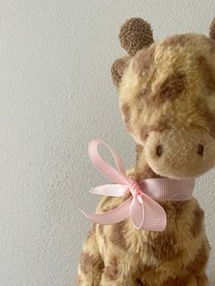 a stuffed giraffe with a pink ribbon on it's neck sits against a white wall