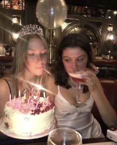 two beautiful women sitting next to each other in front of a cake