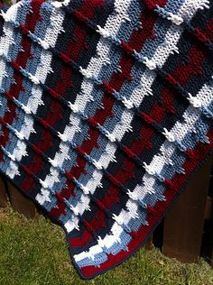 a red, white and blue crocheted blanket sitting on top of a wooden bench