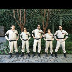 a group of people standing next to each other in front of some trees and bushes