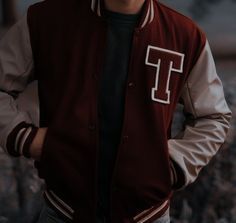 a young man wearing a maroon and white varsity jacket with the letter t on it