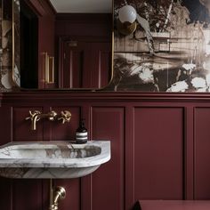 a bathroom with a marble sink and red painted walls, along with gold faucets