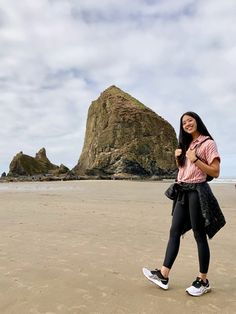 a woman standing on top of a sandy beach next to a large rock in the background