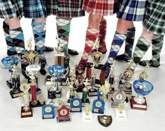 several men in kilts standing next to trophies and plaques on white surface with one man's legs crossed