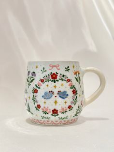 a coffee cup decorated with birds and flowers on it's side, against a white background