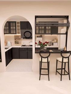 a kitchen with black cabinets and white flooring, two bar stools in front of the counter