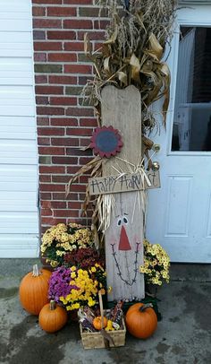 a scarecrow decoration with pumpkins and flowers in front of a house