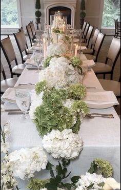 a long table with white and green flowers on it is set for an elegant dinner