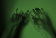 two hands reaching up in the air with their fingers on top of each other, against a green background