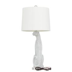 a white table lamp with a cat on it's side and a cord plugged into the base