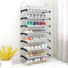 there is a shoe rack with many pairs of shoes on it and a vase full of flowers in the corner