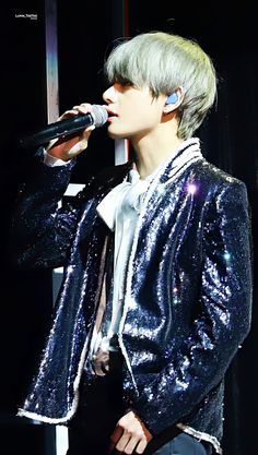 a male in a silver jacket is singing into a microphone