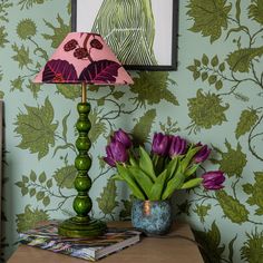 a green lamp sitting on top of a table next to a vase filled with purple flowers