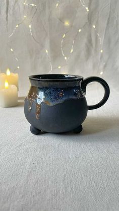 a black mug sitting on top of a table next to a lit candle and some string lights