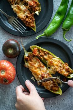 someone is eating stuffed anaheim peppers on a black plate with green peppers and tomatoes in the background