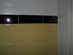 a bathroom with yellow and black tiles on the wall next to a white toilet paper dispenser