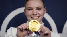 a woman holding up a gold medal in front of a blue and white wall behind her