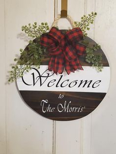 a welcome sign hanging on a door with red and black plaid bow around it's neck