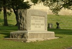 a monument in the middle of a grassy area with trees and gravestones behind it