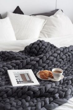 a book and cup of coffee on a bed with a knitted blanket next to it