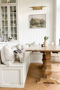 a cat sitting on top of a bench next to a wooden table in a kitchen